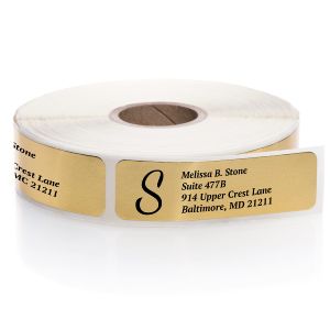 A roll of gold foil address labels showing a personalized monogram and address block template on a shiny metallic background.