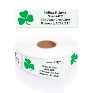 A rectangular personalized address label displayed above a large roll of matching labels, featuring a vibrant green three-leaf shamrock.