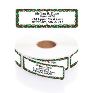A rectangular personalized address label displayed above a large roll of matching labels, showcasing a festive green holly and red berry border.