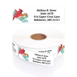 A rectangular personalized address label displayed above a large roll of matching labels, featuring a pair of vibrant red cardinals on a pine branch.