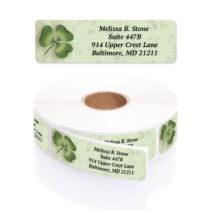 A rectangular personalized address label displayed above a large roll of matching labels, featuring a festive green four-leaf clover wreath.