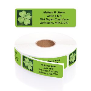 A rectangular personalized address label displayed above a large roll of matching labels, showcasing an artistic green four-leaf clover design.