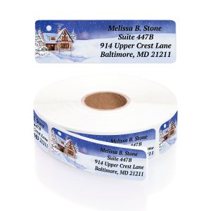 A rolled coil of personalized Winter Cottage return address labels highlighting a cozy snowy cabin artwork and printed contact text.