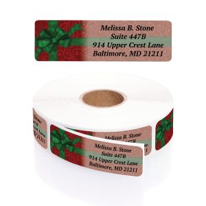 A paper roll of Christmas themed address labels featuring a festive red background, green holly leaf patterns, and a large green gift bow icon.