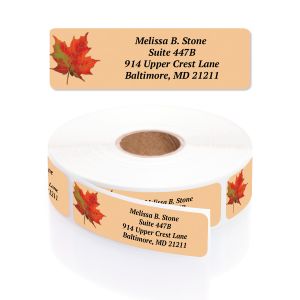 A rectangular personalized address label displayed above a large roll of matching labels, featuring a beautiful red and orange autumn maple leaf.