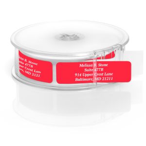 A rectangular personalized address label displayed above a large roll of matching labels, featuring a vibrant ruby-red background with white text.