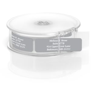 A rectangular personalized address label displayed above a large roll of matching labels, featuring a minimalist grey background with white text.