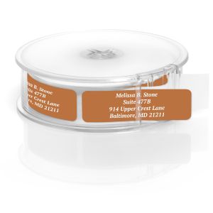 A roll of custom mocha brown address labels in a clear dispenser, showcasing elegant white-printed text lines on a solid warm background.