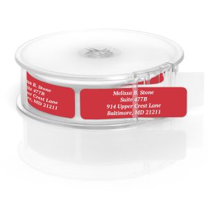A roll of personalized wine-colored address labels housed inside a clear, round plastic dispenser with a single label pulled forward to read.