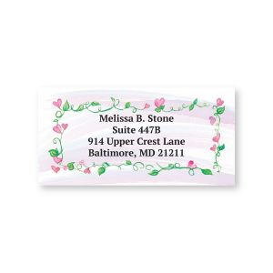A close-up of a rectangular address label framed by a delicate border of green vines, pink leaves, and tiny pink hearts around custom text.
