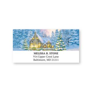 Personalized holiday address label featuring a cozy snow-covered cottage scene with decorated Christmas trees and custom address text lines.