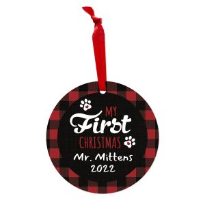 Round metal Christmas ornament with red ribbon, red buffalo plaid border, paw prints, and text reading 