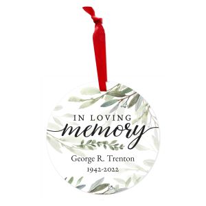 Round metal memorial Christmas ornament with red ribbon featuring greenery foliage, 