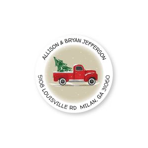A round holiday return address label featuring a nostalgic red truck carrying a Christmas tree, detailed with custom arched typography.