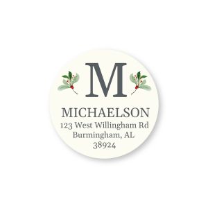 Round ivory address label featuring a large monogram framed by green mistletoe with red berries, above personalized name and address text.