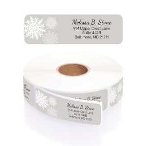 A personalized return address label featuring an elegant white snowflake design on a soft grey background, shown above its matching label roll.