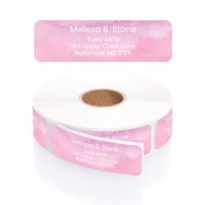 A personalized return address label with a pastel rose pink watercolor background, displayed above its matching roll and clear round dispenser.