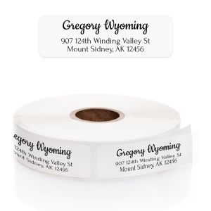 A roll of personalized clear address labels showcasing a modern black script font for the name and a clean serif font for the address.