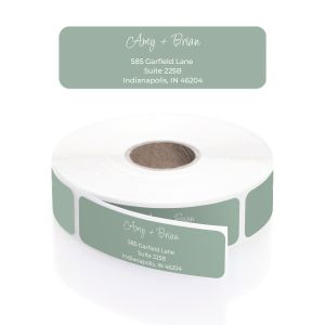A roll of personalized modern sage green address labels showcasing a dainty white script font for names and crisp block text for the address.