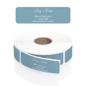 A roll of personalized muted navy blue address labels showcasing a dainty white script font for the names and modern block text for the address.