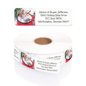 Single personalized address label featuring a marshmallow snowman in a mug displayed above a rolled coil of printed stickers.
