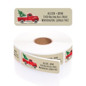 A rectangular personalized address label displayed above a large roll of matching labels, featuring a festive vintage red truck with a Christmas tree.