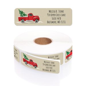 A rectangular personalized address label displayed above a large roll of matching labels, featuring a festive vintage red truck with a Christmas tree.