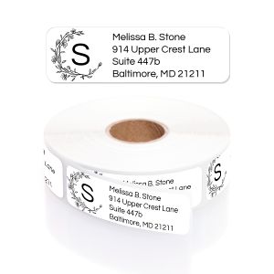 A roll of white address labels featuring a delicate half-floral wreath around a monogrammed letter 