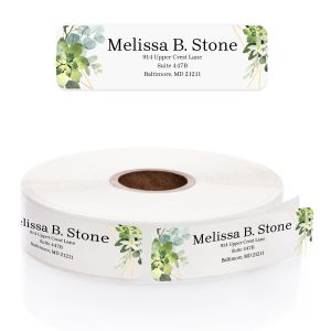 Clear address label with watercolor greenery accents on top and bottom, displayed above a roll of printed personalized return address labels.