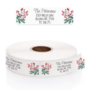 A close-up of a clear rolled address label featuring festive pine branches and red holly berries flanking elegant, custom black text.