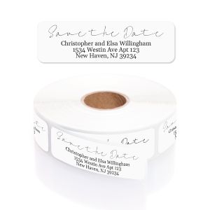 A roll of white Save the Date rolled address labels with cursive header text, peeling slightly to show individual label placement.