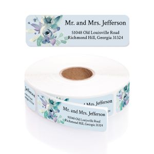 A rectangular personalized address label displayed above a large roll of matching labels, featuring a delicate blue and purple watercolor floral design.